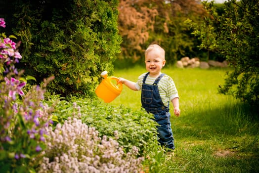 Little baby girl waters plants in backyard garden with watering can