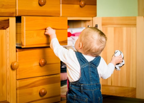 Baby opening drawer with clothes on wooden furniture - home interior