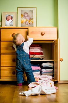 Baby throws out clothes from wooden furniture at home