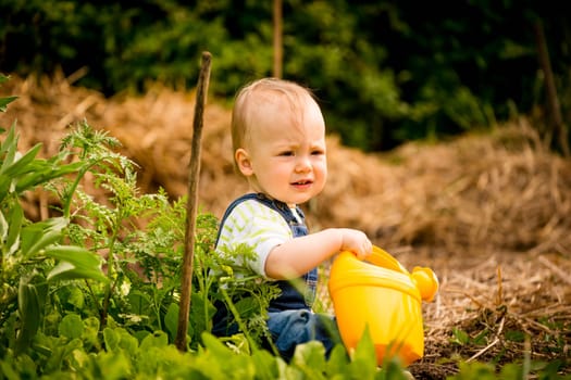 Little baby girl relaxes with watering can in backyard garden