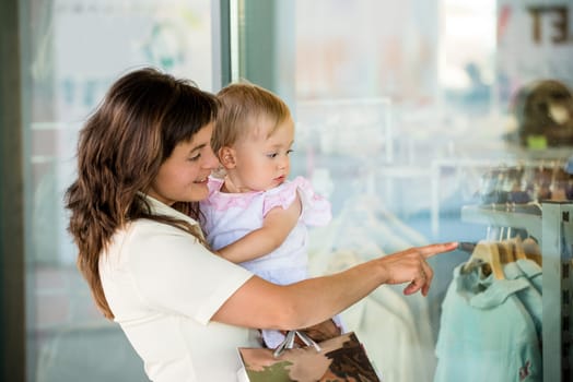 Mother with little girl in white dress looking through shop window