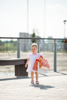 Cute baby goes shopping with bags, outdoor on sunny day