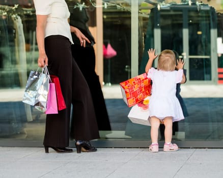 Mother with little girl in white dress looking through shop window