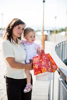 Mother with little girl in white dress holding shopping bags looking somewhere