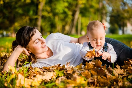Mother lying with her baby in fallen leaves on beautiful autumn day