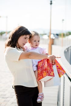 Mother with little girl in white dress holding shopping bags looking somewhere
