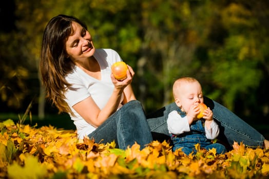 Mother with her cute baby eating apples outdoor in autumn nature