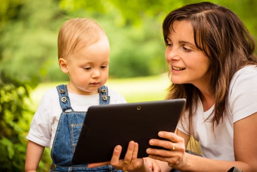 Mother with her baby watching together in tablet computer outdoor