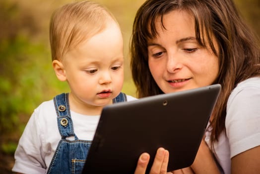 Mother with her baby watching together in tablet computer outdoor