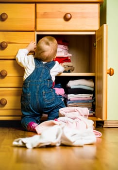 Baby throws out clothes from wooden furniture at home