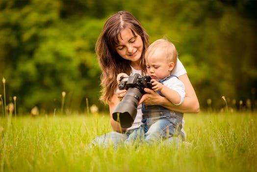 Mother showing her kid captured photos on dslr camera outdoor in nature