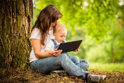 Mother with her child watching together in tablet computer outdoor