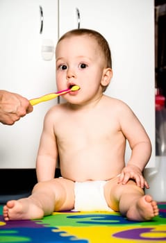 Mother helping clean teeth to her cute baby sitting in bathroom