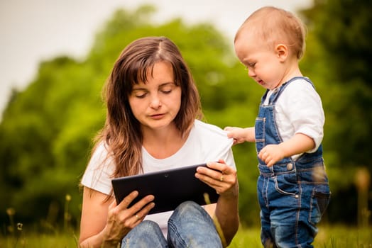 Mother addicted on internet working with tablet while child is trying to draw her attention