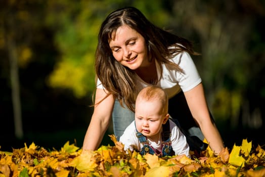 Mother playing with her baby in fallen leaves on fall sunny day