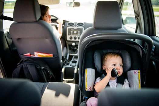 Mother driving car and child sitting on back seat and playing with mobile phone