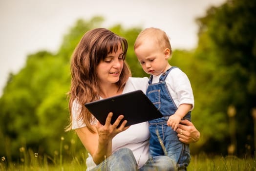 Mother with her baby watching together in tablet computer outdoor