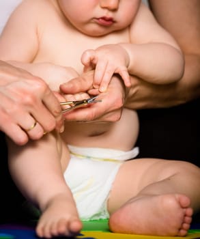Mother cutting nails on hands of her baby - sitting on floor in bathroom