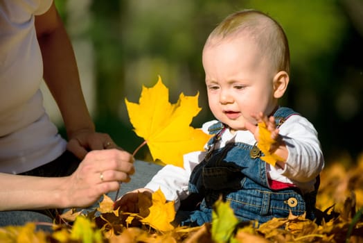 Mother and her baby playing with fallen leaves - outdoor autumn setting