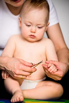 Mother cutting nails on hands of her baby - sitting on floor in bathroom