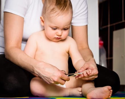 Mother cutting nails on hands of her baby - sitting on floor in bathroom