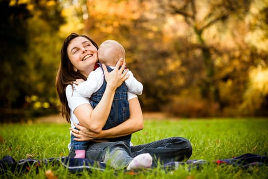 Happy mother holding her baby - sitting outdoor in nature