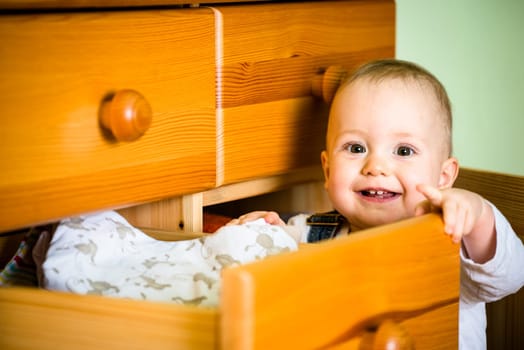 Baby opening drawer with clothes on wooden furniture at home