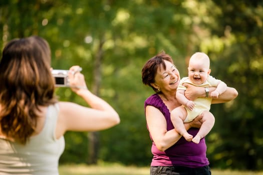 Mother taking photo of grandmother holding her granddaughter - outdoor in nature