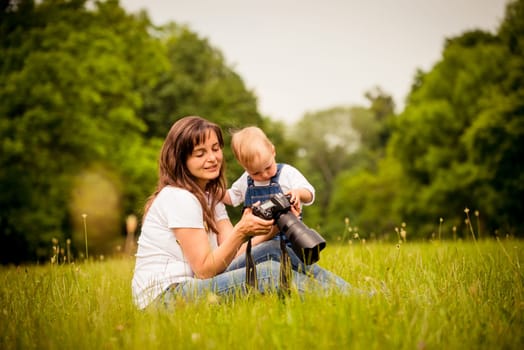 Mother showing her kid captured photos on dslr camera outdoor in nature