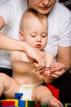 Mother cutting nails on hands of her baby - sitting on floor in bathroom