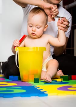 Mother cutting fingernails of her child while baby is playing with toys