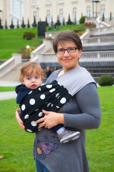 Portrait of mother wearing her baby boy in a sling in the park.