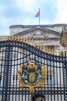 Detail of Buckingham Palace gates with Queen's crest and British flag atop the palace's facade in London, UK