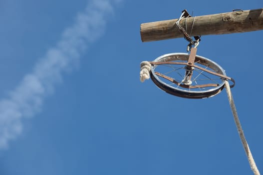 Wheel rim made of a baby trolley with rope over blue sky. It used for the renovation of the facade of the building