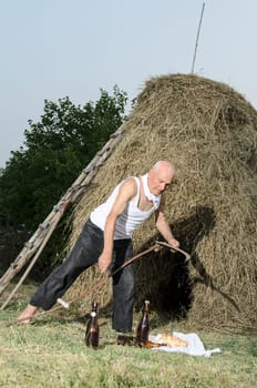 Senior farmer using scythe to mow the lawn traditionally.