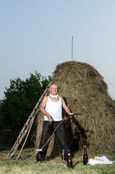 Senior farmer using scythe to mow the lawn traditionally.