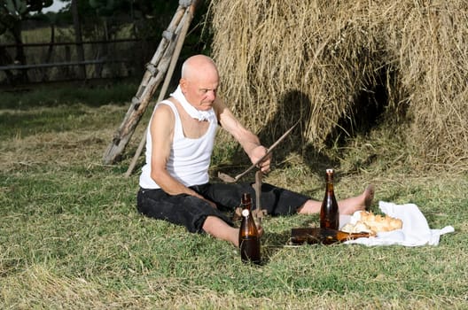 Senior farmer using scythe to mow the lawn traditionally.