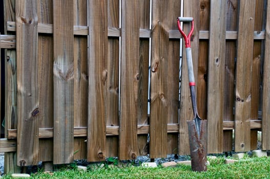 An old rusty shovel is leaning against a wooden fence.