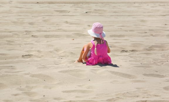 Cute little girl with pink hat sitting with baby doll a hot sunny day on summer vacation and recreation