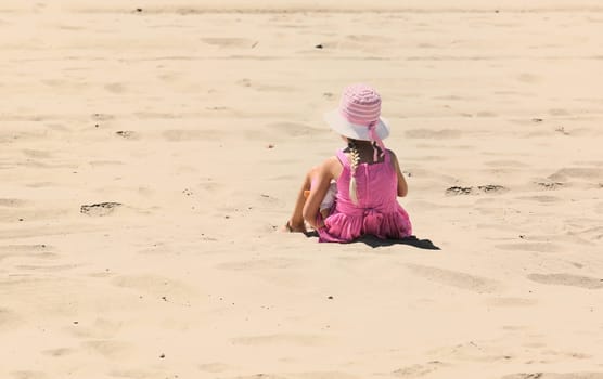 Cute little girl with pink hat sitting with baby doll a hot sunny day on summer vacation and recreation
