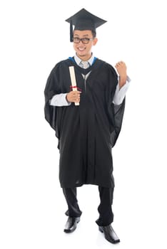 Excited full length Southeast Asian university student in graduation gown, standing isolated on white background.