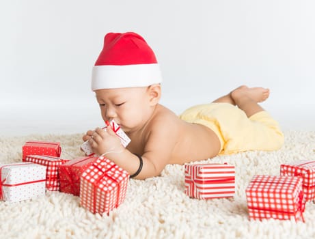 Asian baby boy with santa hat playing with Christmas present on floor.