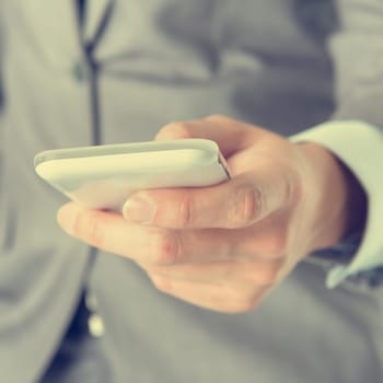 Close-up businessman hand using smart phone in vintage tone.