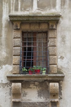 Medieval window with heavy wrought-iron grilles. The plants in red pots are standing on the window sill.