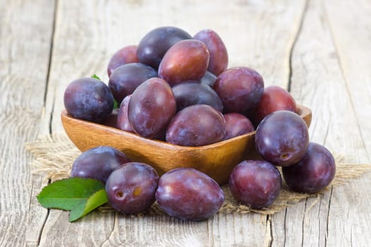 fresh plums in a bowl on old wooden background
