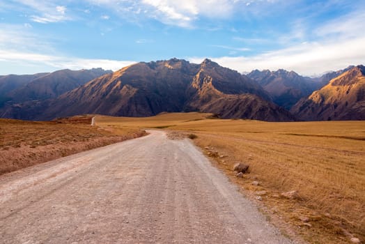 Dirt road with the Andes mountains rising the background in the Sacred Valley near Cusco, Peru