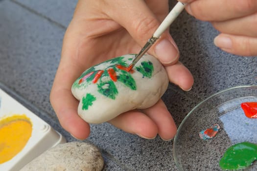 Handmade - stone painting. production decoration. Female hand are drawing picture on the stone.