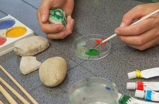 Handmade - stone painting. production decoration. Handmade - stone painting. production decoration. Female hands are dunking brush into the paint. The right hand is holding a stone painted with color.