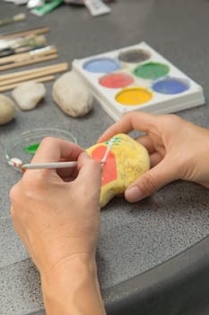Handmade - stone painting. production decoration. Female hand are drawing red heart on the stone. Vertically.