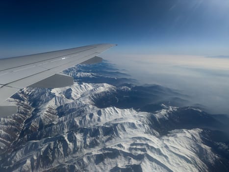 Impeccable view from airplane window while flying over massive mountain ranges in snow. Stunning view from airplane window. The best seats on plane are at wing with beautiful view of mountains